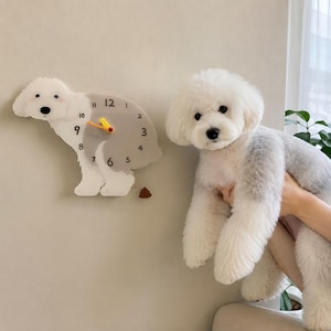 May include: A wall clock shaped like a white and gray dog with a fluffy head and body. The clock face features black numbers from 1 to 12, bright yellow and orange hands, and a small brown icon hanging from the bottom of the dog's body.