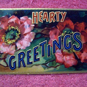 Puede incluir: Postal vintage con ilustraciones florales y las palabras "Hearty Greetings". Las flores son en tonos de rojo, rosa y verde, con un borde dorado. El texto est&aacute; en una fuente estilizada con acentos azules y dorados.