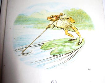 May include: The Tale of Mr. Jeremy Fisher by Beatrix Potter, a vintage children's book cover featuring an illustration of a frog in a white shirt and brown pants, holding a fishing rod and standing on a lily pad in a lake.