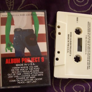 May include: A vintage cassette tape and case. The case features a graphic of a person with green arms and a red, white, and blue background. The text "ALBUM PROJECT 9" is prominently displayed.
