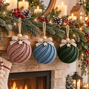 Puede incluir: Tres adornos navideños esféricos con un patrón de punto acanalado texturizado en rosa empolvado, azul apagado y verde oscuro. Cada adorno tiene un lazo de tela beige, una pequeña estrella de madera y un cordel de yute para colgar.