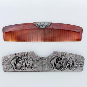 May include: A brown tortoiseshell-style hair comb with a silver-toned metal top accent featuring a decorative floral motif, paired with a separate silver-toned metal protective case embossed with a detailed scene of figures working near a small building.