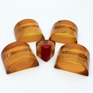 May include: Four semi-circular amber-colored buttons with two holes each, arranged around a single, smaller, triangular-shaped button featuring a deep red center section and translucent amber-colored edges.