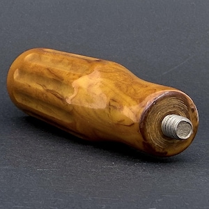 May include: A cylindrical handle with a marbled amber and brown finish, featuring vertical grooves along its length and a threaded metal bolt protruding from one end. The surface has a glossy appearance with a smooth, contoured grip design.