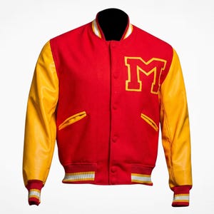 Puede incluir: Una chaqueta universitaria roja con mangas amarillas, que presenta una letra M grande de color amarillo en el pecho izquierdo. La chaqueta tiene cierre frontal con botones a presión, dos bolsillos laterales con ribete amarillo y cuello, puños y dobladillo acanalados con rayas blancas y amarillas.