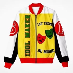 Puede incluir: Una chaqueta bomber con cremallera que presenta un panel frontal amarillo con el texto IDOL MAKER y LET THERE BE MUSIC, junto a máscaras teatrales roja y verde. Las mangas son blancas con parches circulares rojos, paneles negros y cuello rojo.