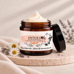 Puede incluir: Un frasco de vidrio marrón lleno de bálsamo de sebo batido blanco, rematado con un remolino. La etiqueta dice ANCESTRA, ALL NATURAL ANCIENT TRADITION FOR MODERN SKIN, CALM, y Whipped tallow balm - Infused with chamomile & lavender, con una ilustración de una vaca.