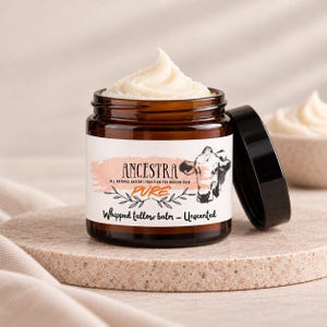 Op de afbeelding: Een amberkleurige glazen pot gevuld met witte opgeklopte talkbalsem, bekroond met een toefje product. Het etiket bevat de tekst ANCESTRA, PURE en Whipped tallow balm - Unscented, naast een zwart-witte illustratie van een koeienkop.