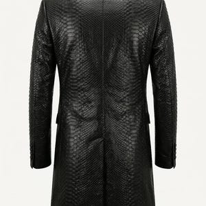 Peut inclure: Un manteau long noir avec un motif texturé en peau de serpent sur toute la surface. Le manteau présente un col structuré, des manches longues avec des poignets boutonnés et une fente centrale au dos, vu de dos.