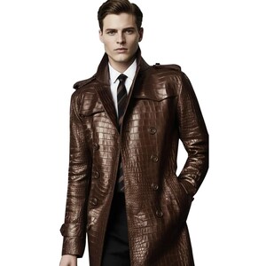 Può includere: Un trench doppiopetto di colore marrone scuro con una trama testurizzata in pelle di coccodrillo. Il cappotto presenta un ampio colletto, spalline e bottoni scuri. Sotto, sono visibili una camicia bianca con colletto e una cravatta scura a righe.