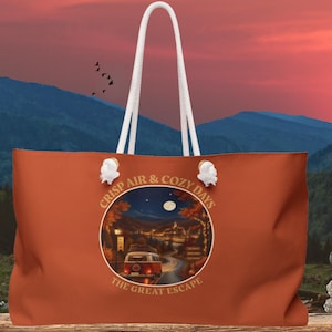 May include: A burnt orange tote bag with white rope handles. The center features a circular graphic of a vintage van on a road at night under a full moon, surrounded by autumn trees. Text reads: CRISP AIR & COZY DAYS THE GREAT ESCAPE.