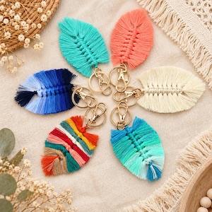Puede incluir: Cinco llaveros de macramé con forma de hoja, equipados con anillas y cierres de mosquetón de metal dorado. Las hojas presentan diversos patrones de color, incluyendo turquesa, coral, crema, un degradado azul y un diseño de rayas multicolor.