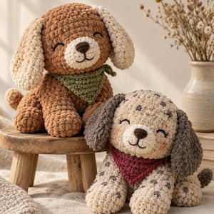 May include: Two plush crochet dog toys with soft yarn textures. One dog is brown with cream ears and a green bandana, while the other is cream with dark gray spots, dark gray ears, and a red bandana. Both have embroidered eyes and noses.