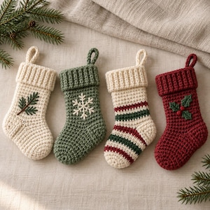 May include: Four small crocheted Christmas stockings with hanging loops. One is cream with a green pine branch, one is sage green with a white snowflake, one has cream, green, and red stripes, and one is deep red with green holly leaves.