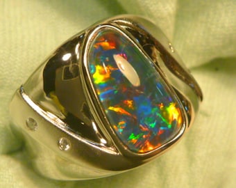 May include: A silver ring with a large, colorful opal gemstone set in a curved, wave-like design. The ring has two small diamonds on the band.