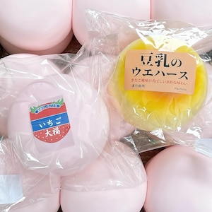 Könnte beinhalten: Eine Sammlung von runden, einzeln verpackten Snacks. Eine Packung enthält einen gelben, kreisförmigen Artikel mit einem Etikett, auf dem 豆乳のウエハース steht. Eine andere Packung zeigt einen rosa, kreisförmigen Artikel mit einem Etikett, das eine Erdbeergrafik und den Text いちご大福 aufweist. Die Artikel sind in einer Gruppe angeordnet.