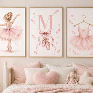 May include: Three wall art prints featuring ballet themes in soft pink tones. The left print shows a ballerina in a tutu, the center print displays the letter M with ballet slippers and a bow, and the right print depicts a tutu on a gold hanger.