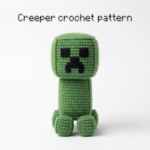 May include: A green crocheted figure with a square head and a cylindrical body, featuring black yarn details for the eyes and mouth. The text "Creeper crochet pattern" is printed in a pixelated black font above the handmade yarn toy.