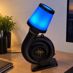 Peut inclure: Une lampe de bureau conçue pour ressembler à un turbocompresseur avec un boîtier noir mat et une roue de turbine dorée. La lampe présente un haut de filtre à air cylindrique et nervuré qui émet une lumière bleue vive, montée sur une base noire plate.