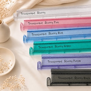 May include: A collection of six rectangular display stands made of translucent material with glitter accents. The stands are labeled Transparent Starry, Transparent Starry Pink, Transparent Starry Blue, Transparent Starry Green, Transparent Starry Purple, and Transparent Starry Black.