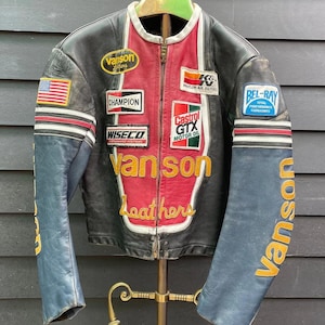 Può includere: Una giacca da moto in pelle nera, rossa e blu con cerniera frontale, colletto bianco e varie toppe ricamate tra cui Vanson, Champion, Wiseco, K&N, Castrol GTX e Bel-Ray. Le maniche riportano il nome del marchio Vanson.