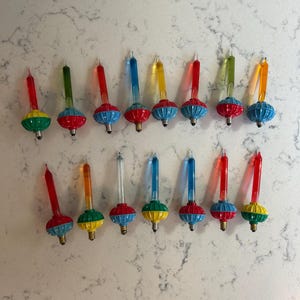 May include: A collection of fifteen vintage-style Christmas light bulbs, each featuring a slender, colored glass filament tube set into a decorative, ribbed, multi-colored plastic base with a small metal screw-in connector at the bottom.