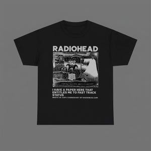 Può includere: Una t-shirt nera a maniche corte con una stampa grafica bianca sul petto. Il design include il testo RADIOHEAD sopra un'illustrazione dettagliata in bianco e nero, con il testo I HAVE A PAPER HERE THAT ENTITLES ME TO FAST TRACK STATUS.