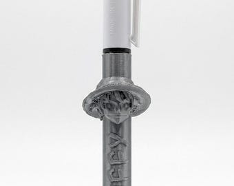 May include: A multi-color ballpoint pen with a white top section featuring red and black ink selectors and the text MADE IN FRANCE. The lower barrel is a metallic gray 3D-printed casing featuring a sculpted character head wearing a hat and the word LUFFY.