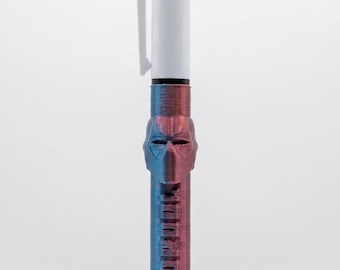 May include: A multi-color ink pen featuring a white top section with red, blue, and green retractable buttons. The lower barrel has a metallic, iridescent purple and blue finish with a sculpted mask design and the word DEADPOOL embossed vertically.
