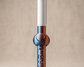 May include: A multi-color ballpoint pen featuring a white top section with four ink color selectors and a metallic blue and copper-toned lower barrel. The lower barrel has a rounded mushroom-shaped grip and the word TOAD embossed vertically.