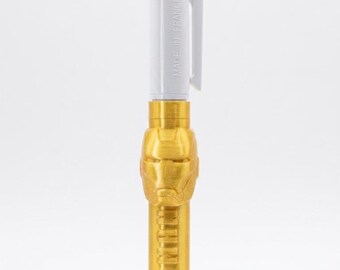 May include: A multi-color ballpoint pen featuring a white top section with a pocket clip and the text MADE IN FRANCE. The lower barrel is gold-colored with a molded Iron Man helmet design and the embossed text IRON MAN along the side of the pen.