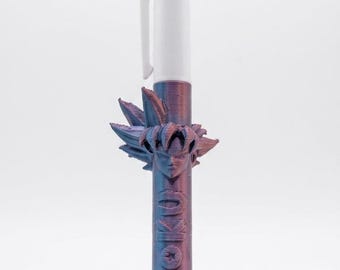May include: A multi-color ballpoint pen featuring a white top section with green and red ink selectors. The barrel is a metallic purple, textured 3D-printed material with a sculpted head of a spiky-haired character and the word GOKU embossed.