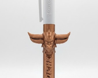 May include: A multi-color ballpoint pen with a white plastic top featuring blue and red ink selectors and the BIC logo. The lower barrel is encased in a metallic copper-colored 3D-printed sleeve shaped like a horned helmet with the text GOLDORAK.