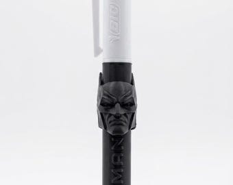 May include: A multi-color ballpoint pen featuring a white top section with green and blue ink selectors and the BIC logo. The lower black barrel is adorned with a three-dimensional Batman mask emblem and the word BATMAN embossed vertically.