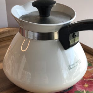 May include: A white ceramic mug with a black handle and the text "But First, Coffee" in a black, bold font. The mug is on a white surface.