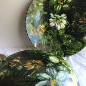 May include: Two decorative items with a floral design. The items feature a green background with white and yellow flowers. The design is repeated on both items, creating a cohesive look. The items appear to be made of a glossy material.
