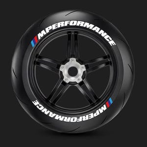 Op de afbeelding: Een zwarte autoband gemonteerd op een zwart vijfspaaks wiel met een zilveren naaf. De zijkant van de band is voorzien van de witte tekst MPERFORMANCE en een blauwe, paarse en rode streepafbeelding aan zowel de boven- als onderzijde.