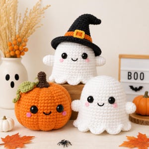 Può includere: Due fantasmi all'uncinetto bianchi e una zucca all'uncinetto arancione. Un fantasma indossa un cappello da strega nero con una fascia arancione e una fibbia gialla. Ogni figura ha occhi neri, un sorriso ricamato e guance rosa. Un piccolo ragno nero.