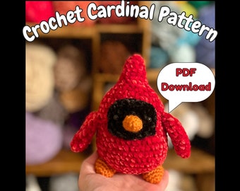 May include: Crochet pattern for a red cardinal bird with black eyes and an orange beak. The pattern is available as a PDF download.