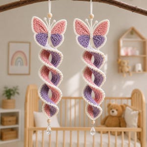 May include: Two hanging crochet butterfly decorations featuring a spiral tail design. Each butterfly has pink and purple wings with white trim, a wooden bead at the top, and a clear crystal-like teardrop pendant hanging from the bottom of the spiral.