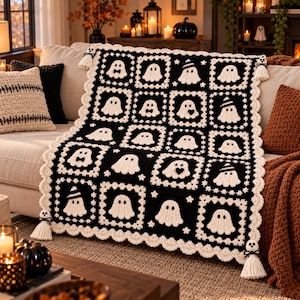 Può includere: Una coperta all'uncinetto bianca e nera con un motivo ripetuto di fantasmi all'interno di blocchi quadrati. La coperta presenta un bordo smerlato color crema e quattro nappe agli angoli, ciascuna sormontata da una piccola figura di fantasma.