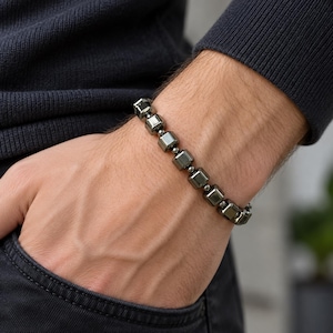 May include: A bracelet featuring a series of polished, dark metallic cube-shaped beads alternating with small, round spherical spacers. The beads have a reflective, gunmetal gray finish and are strung together in a single continuous line.