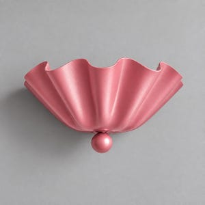 Op de afbeelding: Een matte roze wandlamp met een brede, gegolfde, schelpachtige kap met diepe, verticale plooien. Het armatuur is gecentreerd rond een klein, bolvormig detail aan de basis, wat een symmetrisch, komvormig silhouet creëert.