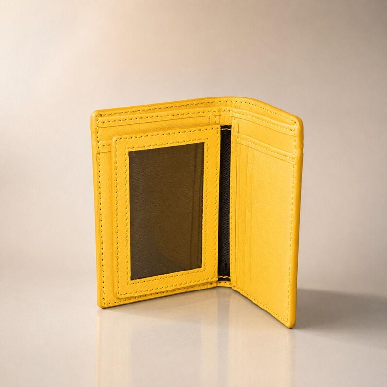 May include: A bright yellow bi-fold wallet featuring a clear rectangular ID window on the left interior panel and multiple vertical card slots on the right interior panel, with visible tonal stitching along the edges of the wallet structure.