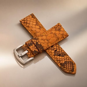 Könnte beinhalten: Ein Uhrenarmband mit einer strukturierten, orangefarbenen und braunen Schlangenhaut-Optik. Das Armband verfügt über eine silberfarbene Metallschnalle und eine Reihe von gestanzten Löchern zur Anpassung mit detailliertem Schuppenmuster.