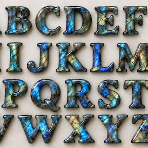 May include: A complete set of twenty-six alphabet letters from A to Z, crafted from polished labradorite stone. Each letter features a smooth, rounded surface with a distinct iridescent blue and gold colour pattern, showcasing natural mineral veining.