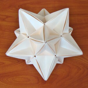 May include: A white origami star with a 3D geometric design. The star is made of paper and has a pointed shape.