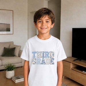 Könnte beinhalten: Ein weißes kurzärmeliges T-Shirt mit dem Schriftzug "THIRD GRADE" in Blockbuchstaben. Die Buchstaben haben ein blau-weißes Muster aus kleinen Blumenprints, Vichy-Karos und Punkten, was ein dekoratives grafisches Design ergibt.