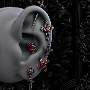 May include: A set of black metal ear piercings featuring red gemstone accents. The collection includes a sword-shaped industrial bar, a cross-shaped stud, a round prong-set red stone, a heart-shaped cross, and a dangling cross charm with red stones.