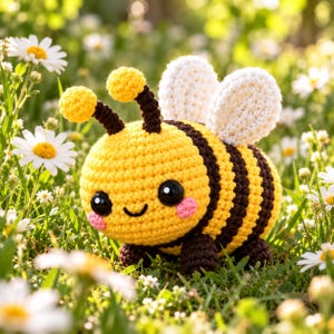 May include: A crocheted bee toy featuring a round yellow body with horizontal dark brown stripes, two white textured wings, and two antennae topped with yellow spheres. The bee has large black safety eyes and pink cheeks.